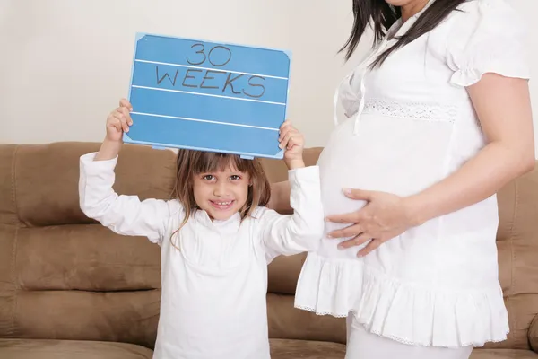 Girl holding a 30 weeks sign to her expectant mother — Stock Photo, Image