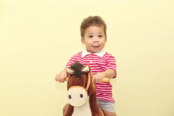 Retrato de um menino africano adorável em seu brinquedo de cavalo . — Fotografia de Stock