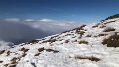 Güneşli bir kış gününde bulutların üzerinden görünen bir manzarayla uçurumların yanında yürümek