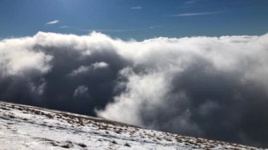 Kabarık bulutlar bir dağın yamaçlarına doğru hareket ediyor.