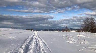 Güneşli bir kış gününde dağların kırsalında karlı yolda yürüyorum.
