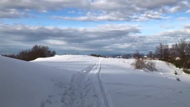 Güneşli bir kış gününde dağların kırsalında karlı yolda yürüyorum.