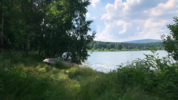 在一个阳光明媚的夏日 在一个高山湖畔的草地上散步 看到远处的渔船上有许多渔民 — 图库视频影像
