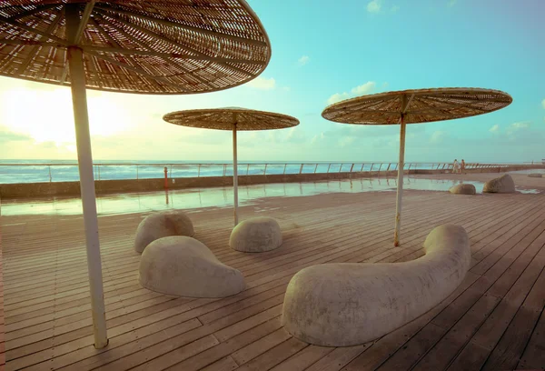 Деревянная палуба с каменными скамейками и металлом с соломенными зонтами Стоковое Изображение