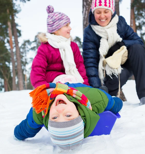 Zwei Kinder rodeln mit der Mutter in der Winterlandschaft. Fokus auf den Jungen. — Stockfoto