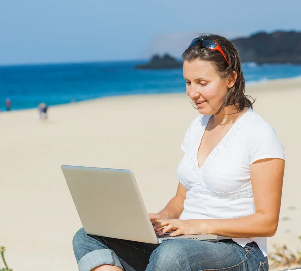 Dizüstü bilgisayar ile sahilde oturan kadın — Stok fotoğraf