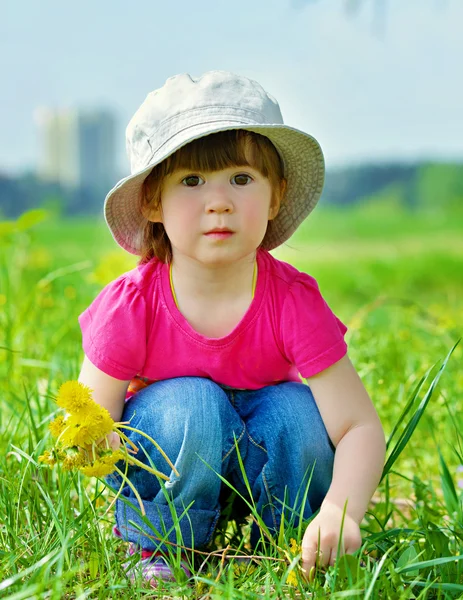 Meisje zit onder paardebloemen — Stockfoto