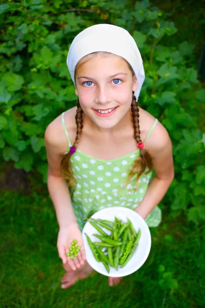 Mooi meisje houden plaat van groene erwten in tuin — Stockfoto