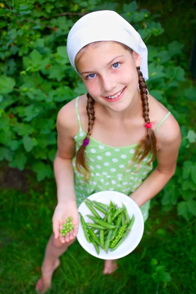 Krásná dívka drží talíř zelený hrášek v zahradě — Stock fotografie