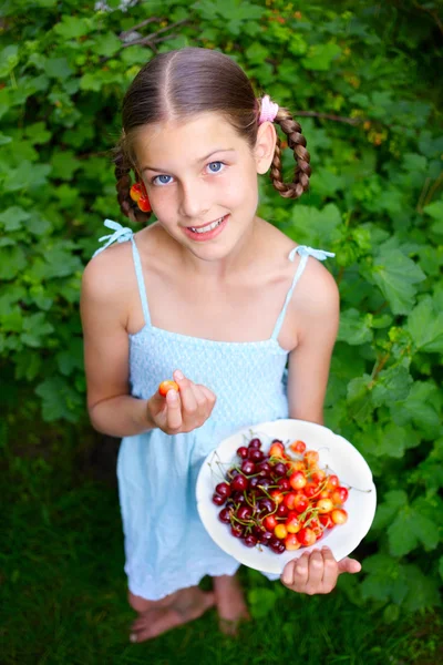 Krásná holčička usmívající se jíst třešně v zahradě — Stock fotografie