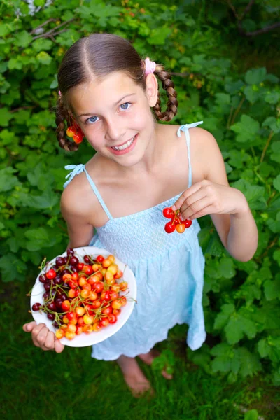 Linda menina sorridente comendo cerejas no jardim — Fotografia de Stock