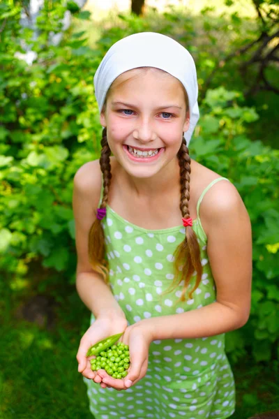 Portret van mooi meisje houdt van groene erwten in tuin — Stockfoto