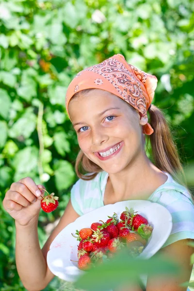 Linda menina sorridente comendo morangos no jardim — Fotografia de Stock