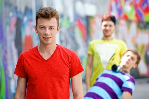 Портрет счастливого мальчика-подростка со своими друзьями за нарисованной стеной, смотрящего в камеру. Вертикальный вид — стоковое фото