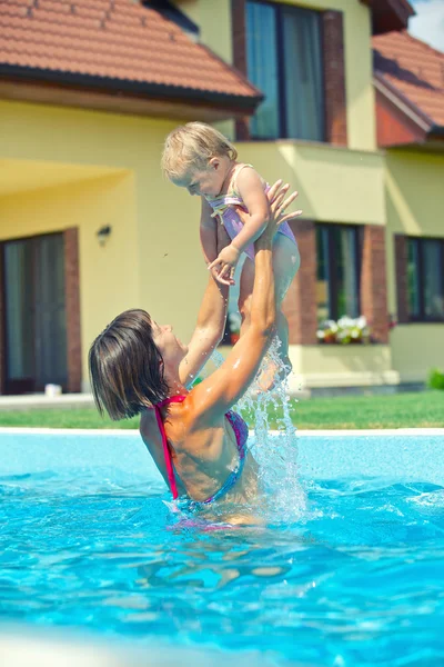 Летние каникулы. Молодая женщина колет со своей маленькой дочерью в бассейне на открытом воздухе — стоковое фото