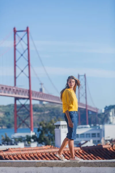 Portugal turistattraktioner koncept. Attraktiv brunett flicka und 25 April Bridge i Lissabon Royaltyfria Stockbilder
