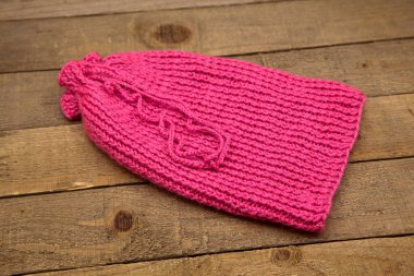 El yapımı yün örgü. Ahşap arka planda izole edilmiş pembe şapka.