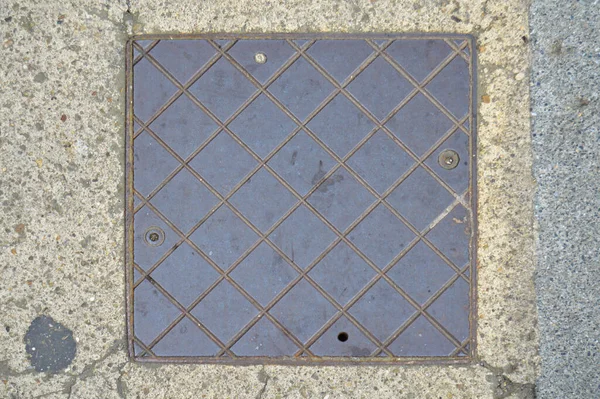 コンクリートで固定された床の上に古い金属製の正方形のマンホールカバー — ストック写真