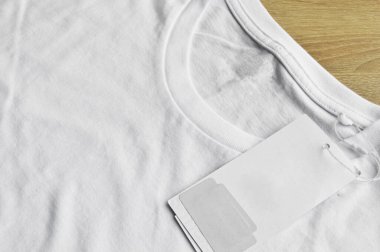 Beyaz temiz mavi tişört ve boş etiket, ahşap zeminde.