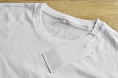 Beyaz temiz mavi tişört ve boş etiket, ahşap zeminde.