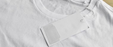 Beyaz temiz mavi tişört ve boş etiket, ahşap zeminde.