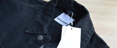 Siyah kot ceket ve boş etiket kağıdı, ahşap zeminde.