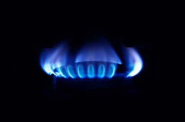 Mutfakta gaz ocağı yanıyor, siyah arka planda mavi alevler izole edilmiş.