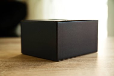 Closed black rectangular cardboard box with corrugated cardboard lid, on oak wooden table