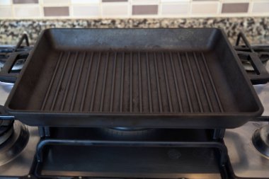 Boş siyah döküm, modern bir mutfakta gaz ocağında ağır demir ızgara tavası.