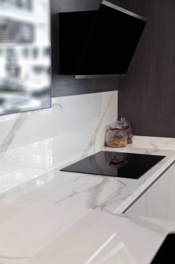 Modern gri beyaz laquer ahşap mutfak ekipmanı ve siyah elektrikli soba ve beyaz granit tezgahta kaput