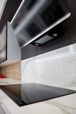 Modern gri beyaz laquer ahşap mutfak ekipmanı ve siyah elektrikli soba ve beyaz granit tezgahta kaput