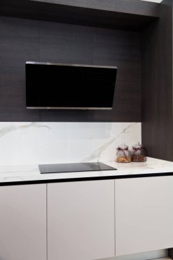 Modern gri beyaz laquer ahşap mutfak ekipmanı ve siyah elektrikli soba ve beyaz granit tezgahta kaput