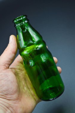 Gri arka planda izole edilmiş üç temiz yeşil boş soda şişesi ve el.