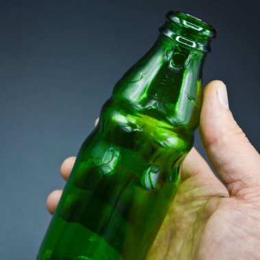 Gri arka planda izole edilmiş üç temiz yeşil boş soda şişesi ve el.
