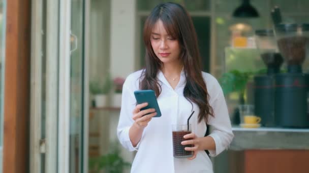コーヒーショップでスマートフォンを使っている美しい若いアジアの女性、幸せな笑顔 — ストック動画