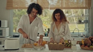 Genç, mutlu, evli çift dans ediyor. Birlikte gülüyorlar. Evde yemek pişiriyorlar. Kaygısız, neşeli karı koca, Boho tarzı mutfakta sağlıklı kahvaltı hazırlıyorlar.