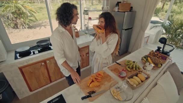 Junge glückliche aktive Ehepaare tanzen lachend zusammen und kochen zu Hause Mahlzeiten, unbeschwert fröhliche Eheleute haben Spaß beim Kochen gesunder Frühstücksspeisen in Boho-Küche — Stockvideo