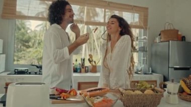 Genç, mutlu, evli çift dans ediyor. Birlikte gülüyorlar. Evde yemek pişiriyorlar. Kaygısız, neşeli karı koca, Boho tarzı mutfakta sağlıklı kahvaltı hazırlıyorlar.