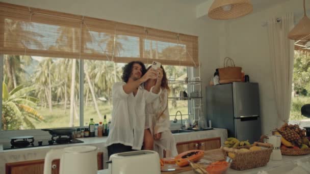 Молода щаслива пара бере селфі під час приготування їжі — стокове відео