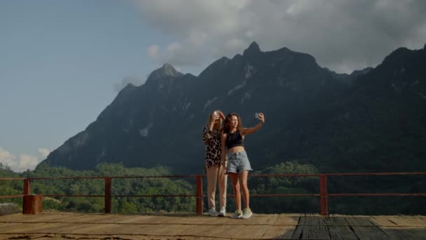 Duas jovens fotografadas contra a vista da montanha, desfrutando de suas férias, aventura de viagem. — Vídeo de Stock
