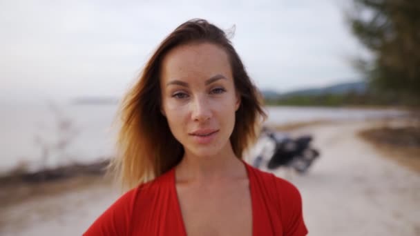Молодая женщина в красном купальнике стоит на заднем плане с мотоциклом — стоковое видео
