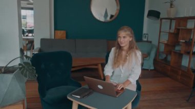 A blonde woman works on her laptop at a coffee shop. A female freelancer works remotely.