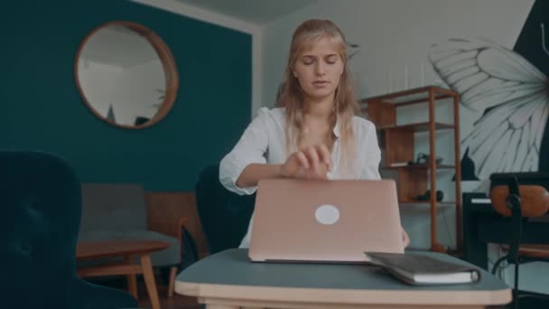 A blonde woman works on her laptop at a coffee shop. A female freelancer works remotely. — Video