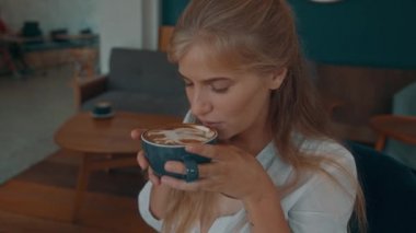 Woman is enjoying her cup of coffee sitting at coffee shop.