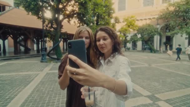 Two young smiling girls take selfie photos on a smartphone. Models pose in front of the street. — Video Stock