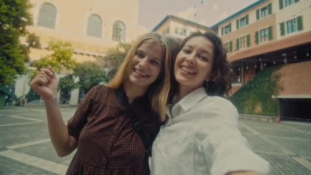 Two young smiling girls take selfie photos on a smartphone. Models pose in front of the street. — Wideo stockowe