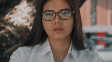 Asyalı çekici, gözlüklü genç bir kadın, dışarıda bir teras kafede laptopunun başında çalışıyor.