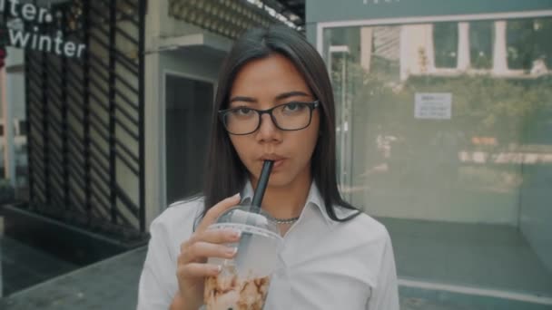 Retrato tiro de um asiático atraente jovem mulher vestindo óculos beber café frio fora — Vídeo de Stock