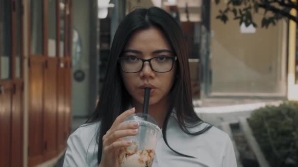 아시아의 매력적 인 한 젊은 여자 가 바깥에서 시원 한 커피를 마시고 있는 모습 — 비디오