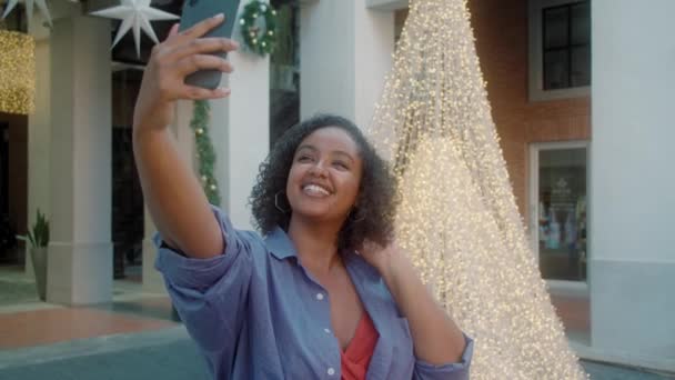 Hermosa mujer afroamericana de moda tomando selfies en la calle contra el árbol de Navidad — Vídeo de stock